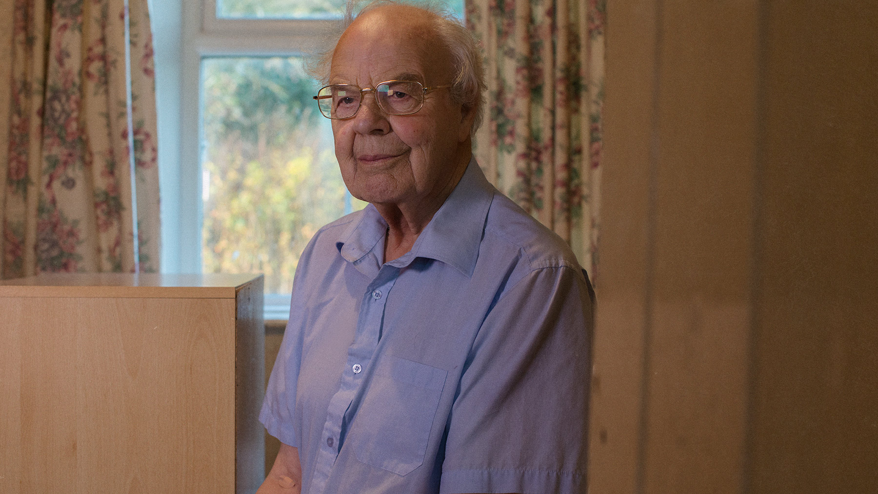 Good Boy Wolf Photographer, filmic portrait, old man wearing blue shirt sitting on his bed 