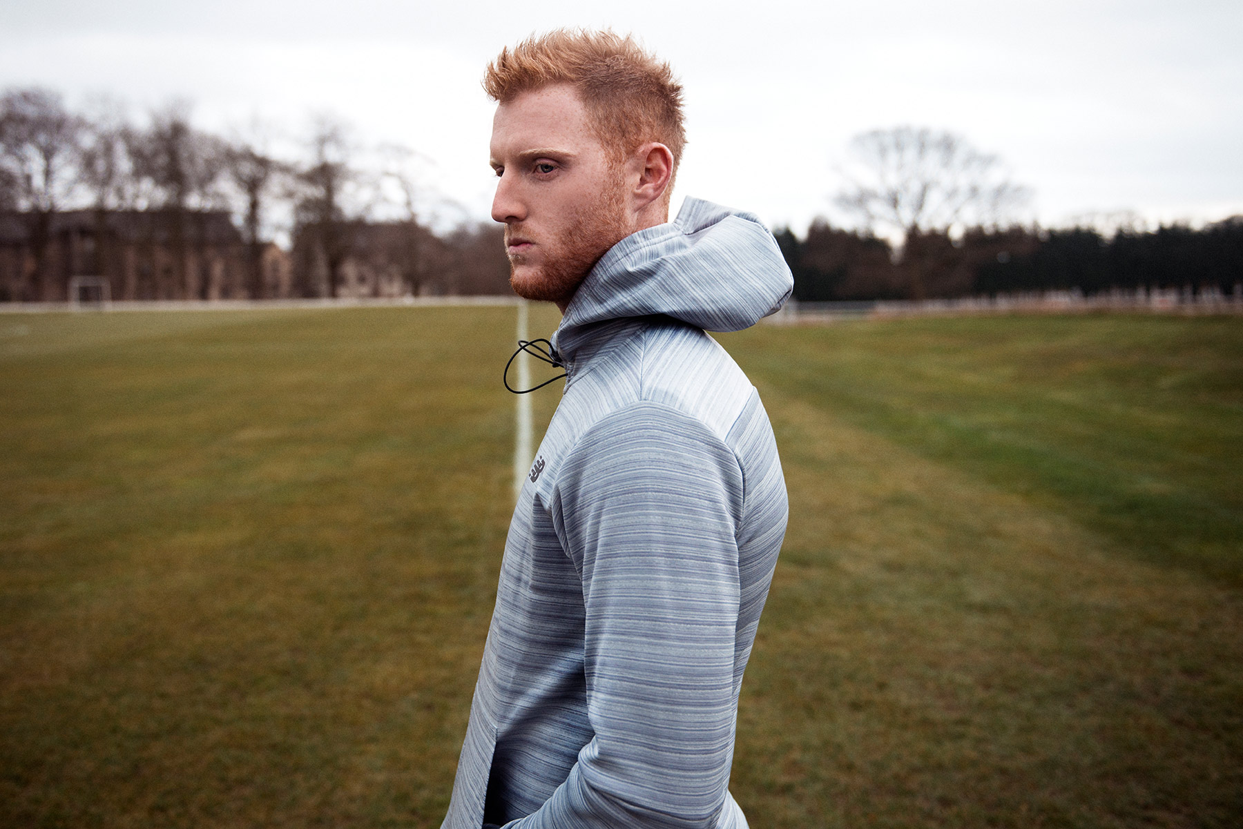 Good Boy Wolf Photographer, filmic portrait, ben stokes cricketer standing in a field wearing grey top 