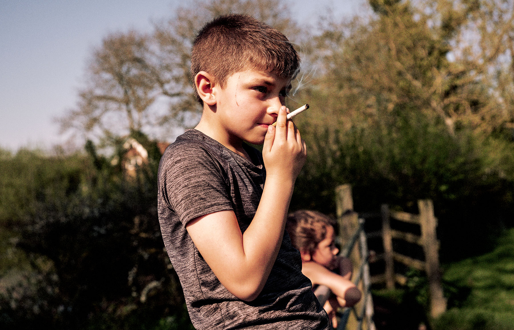 Good Boy Wolf Photographer, young boy smoking a cigarette on a fence 