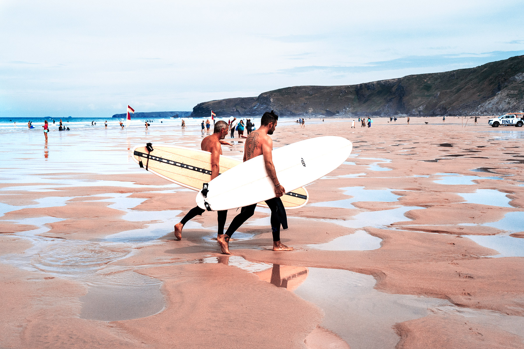 Good Boy Wolf Photographer, filmic portrait, two surfers walking on wet sand 